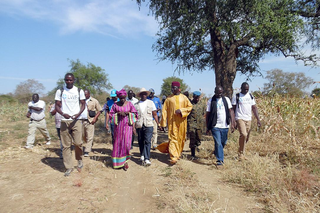 Mitarbeiter und Mitarbeiterinnen und die vor Ort lebenden Menschen besichtigen gemeinsam mit Besucherinnen und Besuchern die Felder des Projekts im Bezirk Kimiti. Foto: LWB Tschad