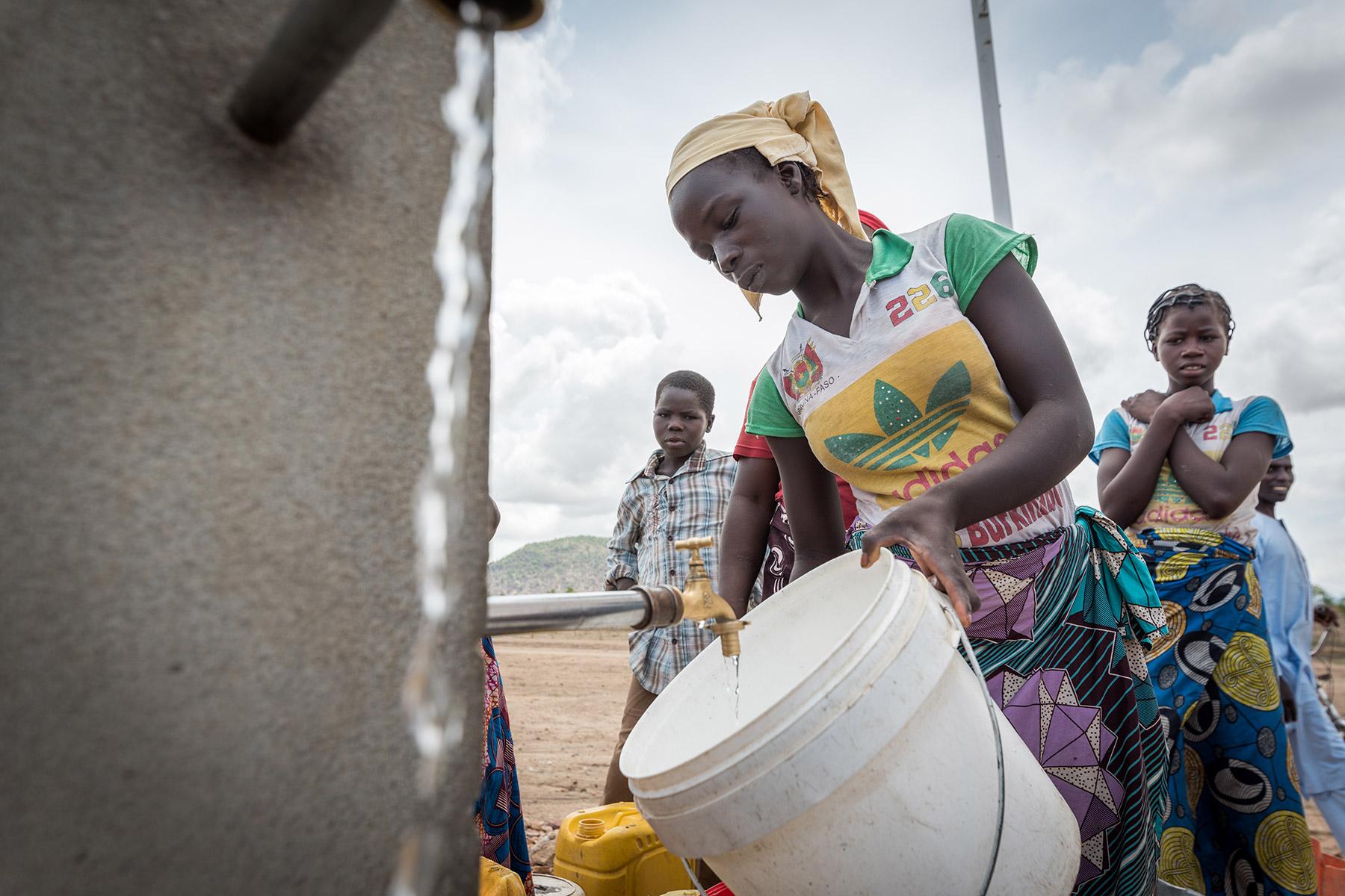 Für die schwächsten und gefährdetsten Bevölkerungsgruppen ist der Zugang zu ausreichend sauberem Trinkwasser in Zeiten des Klimawandels, aber auch in der Corona-Pandemie von zentraler Bedeutung. Eine junge Frau steht im Flüchtlingslager Minawao an, um ihren Eimer an einer der gemeinschaftlichen Wasserzapfstellen mit Wasser zu füllen. In dem Flüchtlingslager für nigerianische Flüchtlinge im äußersten Norden des Kamerun leben derzeit rund 58.000 Flüchtlinge aus Nordostnigeria. Unterstützung erhalten die Flüch