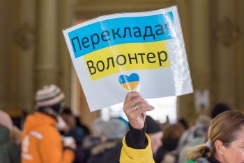 A woman holds up a sign offering practical support for newly arrived families from Ukraine, at Nyugati station in Budapest, Hungary. At the station, a range of civil society organisations and other volunteers offer support to incoming refugees, including support in arranging free accommodation, tickets for onward travel, as well as necessary items such as snacks and food, diapers for the children, clothes and basic medical supplies. Photo: LWF/Albin Hillert