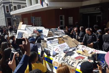 The anti-femicide demonstration in Cape Town, South Africa following the death of Uyinene Mrwetyana. Protestors cover a police vehicle with placards. Photo: Discott, via Wikimedia Commons (CC-BY-SA)