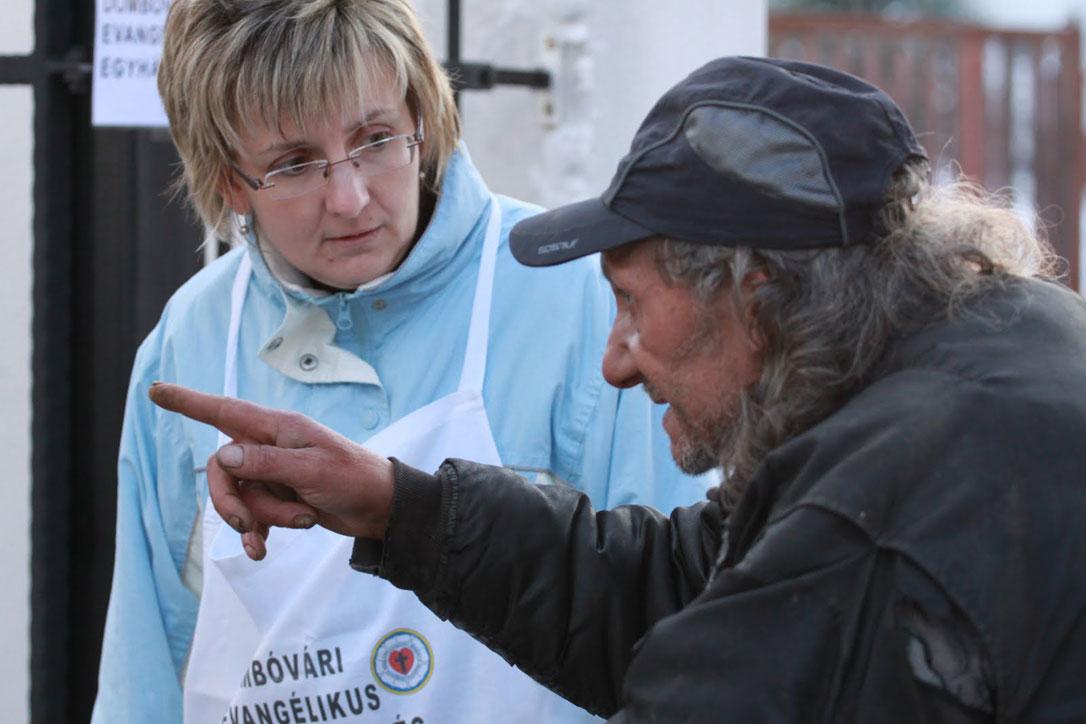 Social worker Anita VÃ¡rkonyi listens to a man in DombÃ³vÃ¡r, Hungary, where the Lutheran diaconal organization provides services, such as hot meals in winter. Photo: LWF