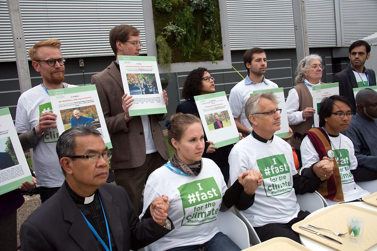 An interfaith group of religious leaders sits in front of empty trays during a public action at COP21 in Paris in 2015. Photo: LWF/Ryan Rodrick Beiler
