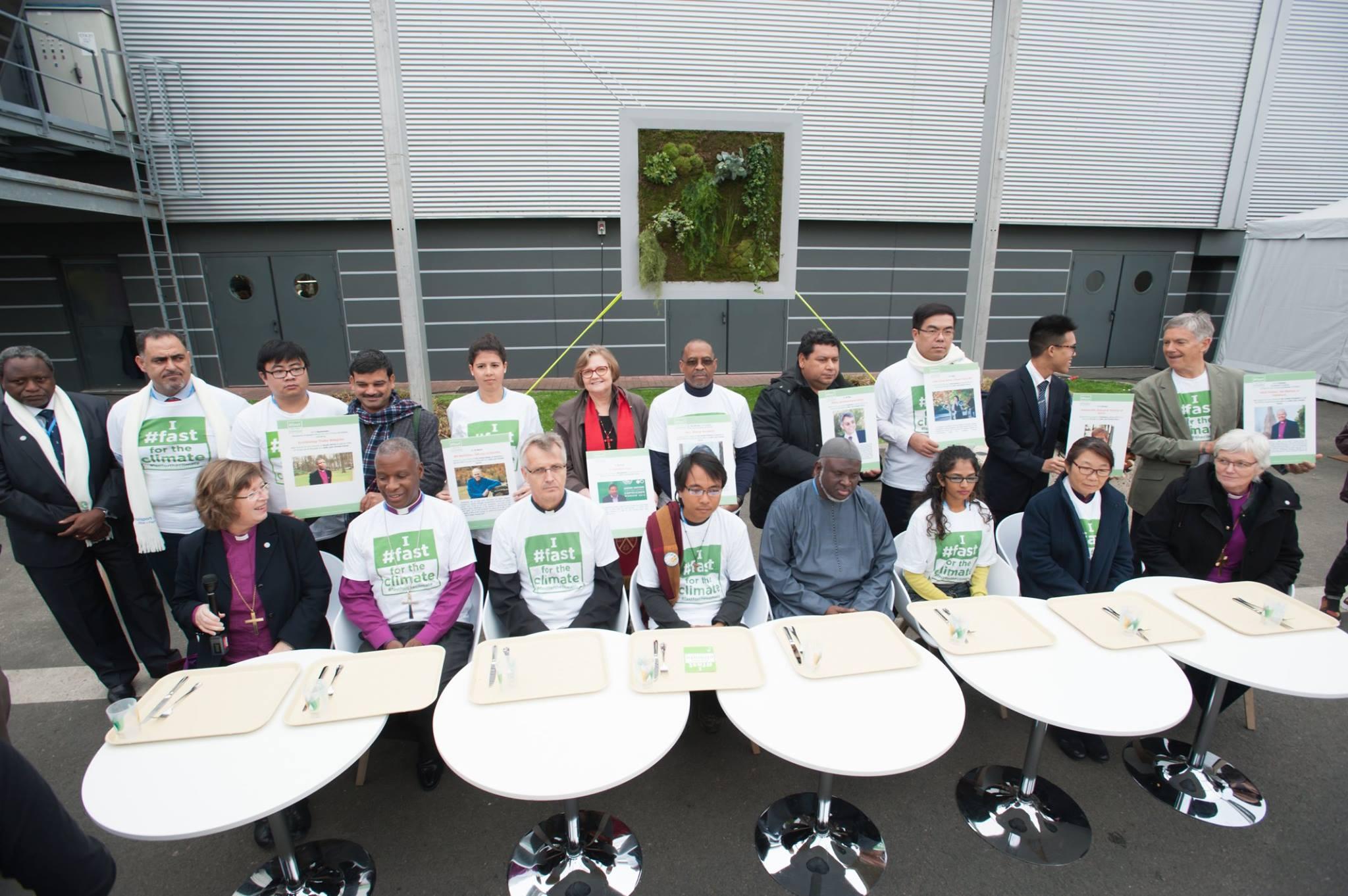 An interfaith group of religious leaders sits in front of empty trays during a public action promoting the Fast for the Climate campaign during the COP21 UN climate summit in Paris, France. Photo: LWF/R. Rodrick Beiler