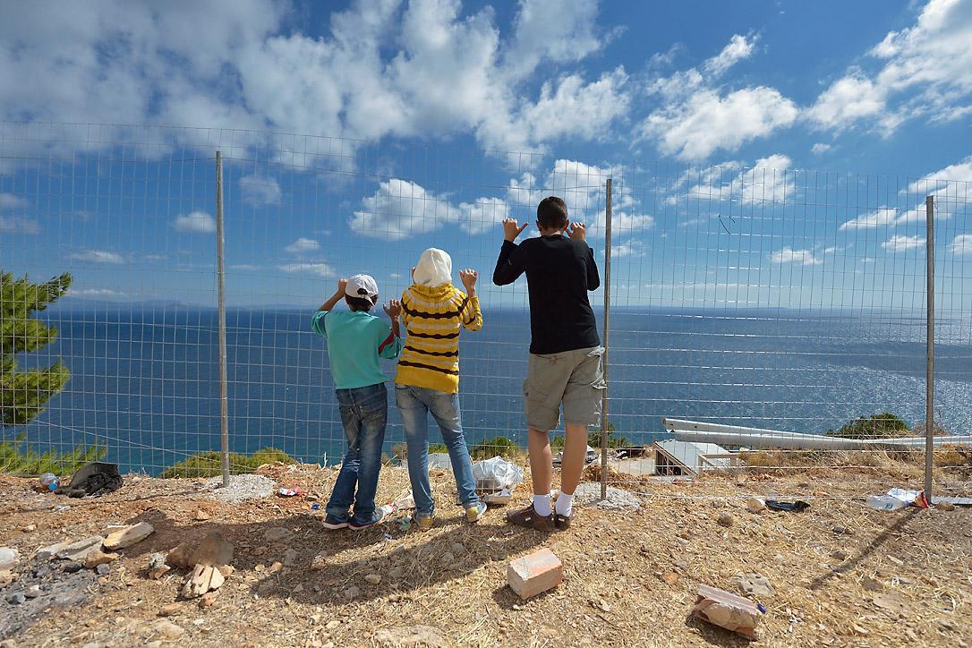 Syrische Flüchtlingskinder blicken durch einen Zaun über die Ägäis, Griechenland. Foto: ACT/ Paul Jeffrey