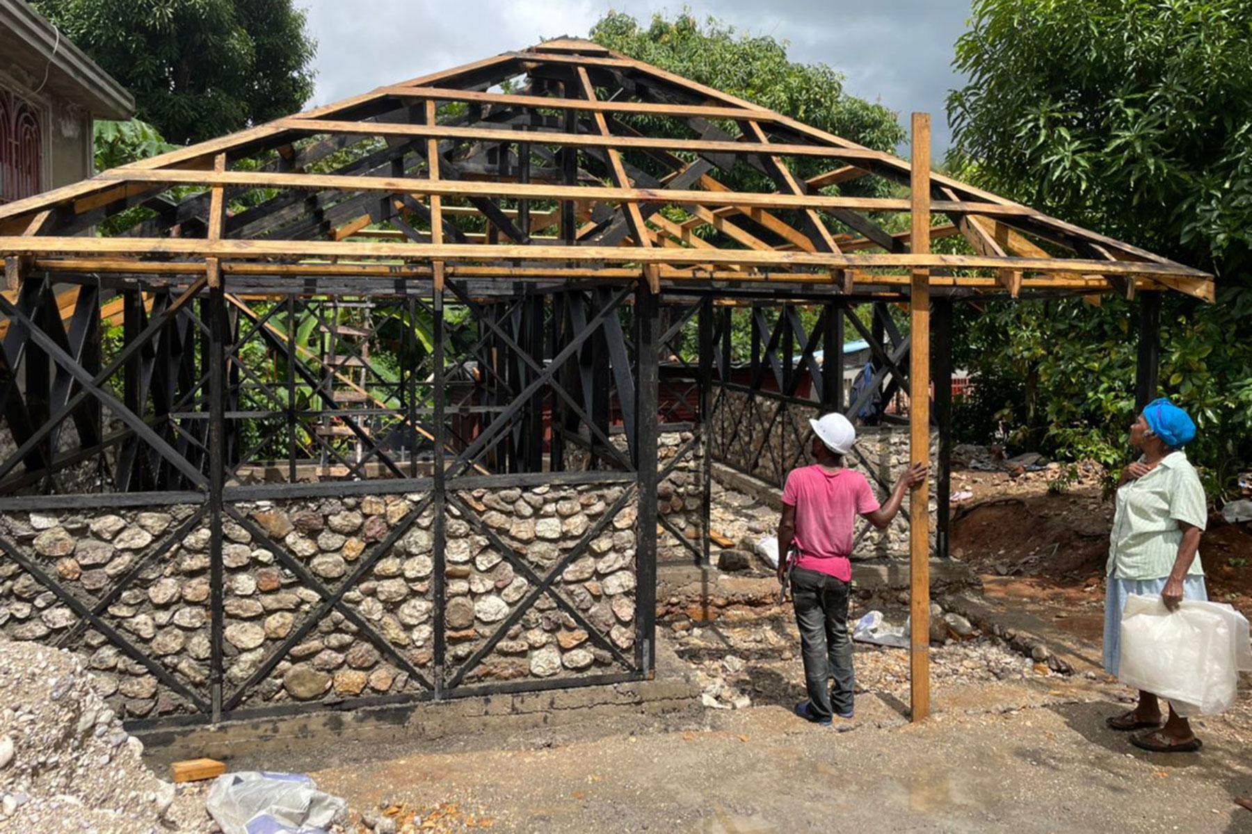 Im Rahmen des Wohnungsbauprojekts stellen die Teilnehmenden Steine, Holz und Lebensmittel für die Bauarbeiter zur Verfügung. Marie Nusia, eine Projektteilnehmerin, beobachtet den Fortschritt beim Bau ihres neuen hurrikan- und erdbebensicheren Hauses. Foto: LWB Haiti