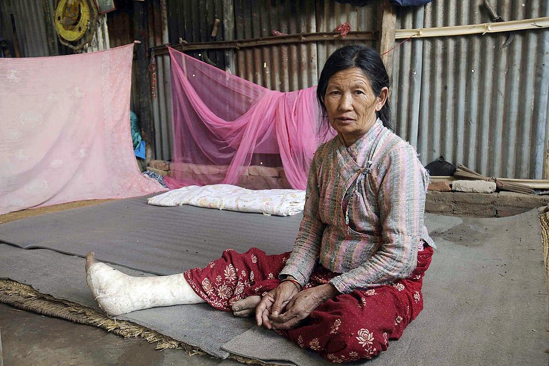 Kanchi Shrestha, 71, mit versorgtem Beinbruch vor ihrer Notunterkunft. Der LWB hat Shrestha und ihrer Familie geholfen und unterstützt sie auch beim Wiederaufbau ihrer Häuser. Foto: LWB Nepal