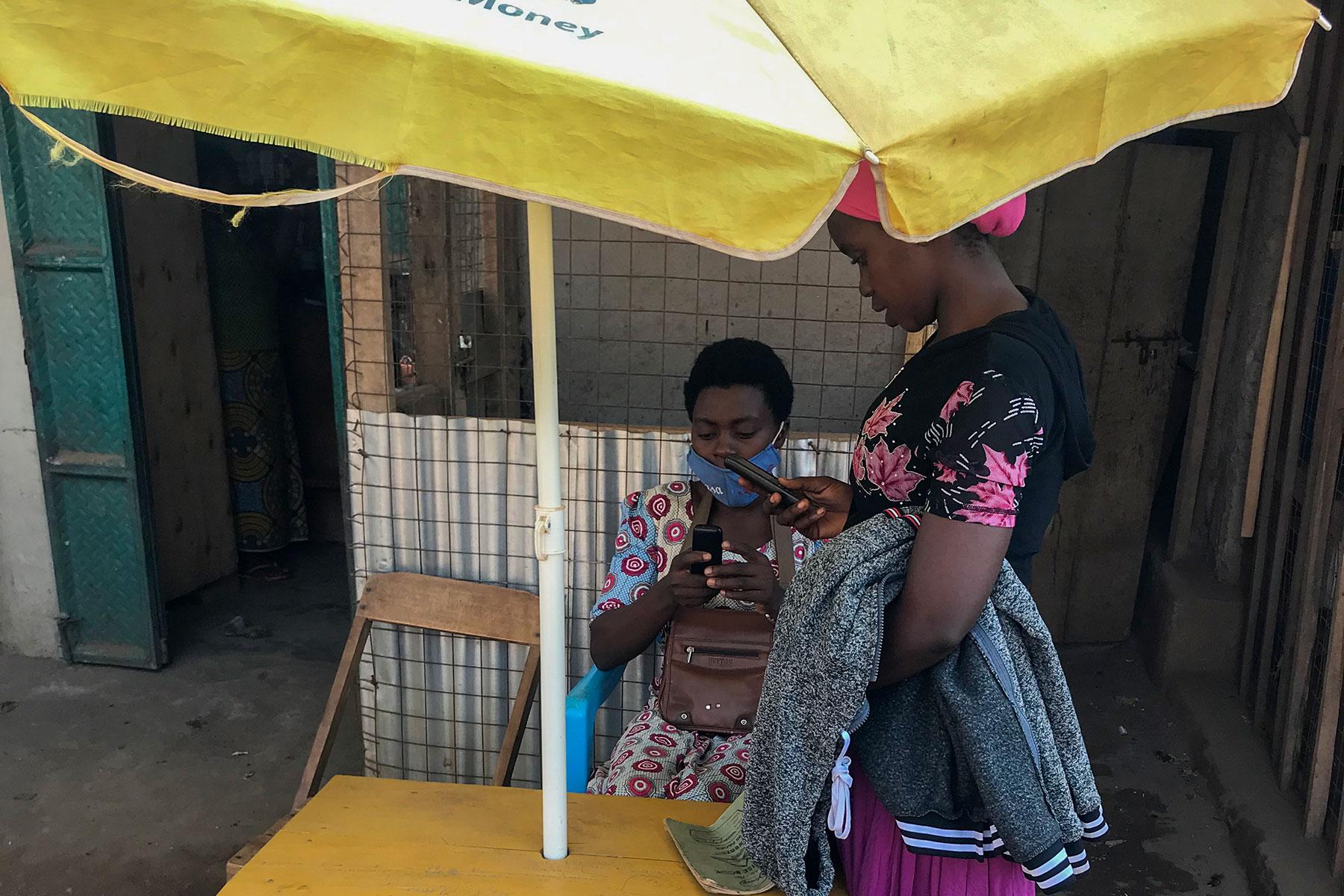 Vestina betreut eine Kundin bei ihrem Geschäft für mobiles Bezahlen in der Kyangwali-Flüchtlingssiedlung. Foto: LWB-Uganda