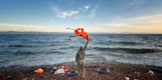A Greek volunteer waves at a refugee boat in the Aegean Sea, directing it toward a safe place to land on a beach on the Greek island of Lesbos. Photo: Paul Jeffrey