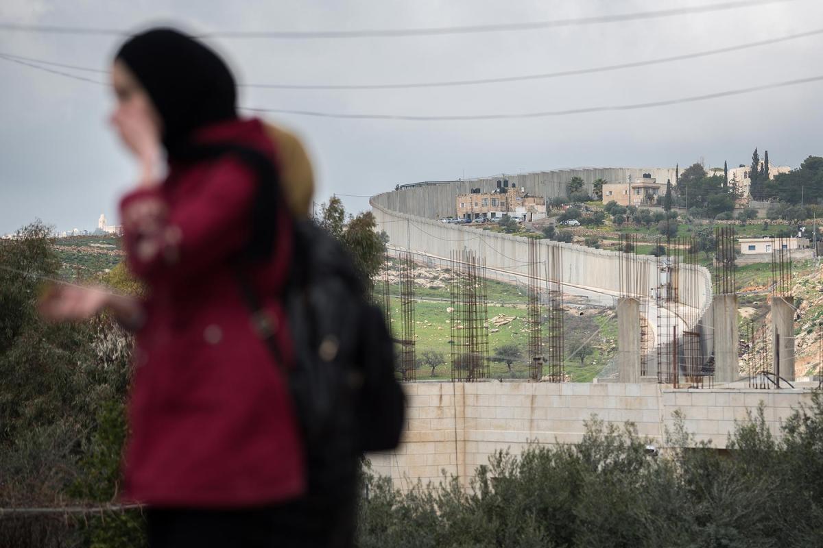 In Abu Dis, Palestine, 2020: A woman walks toward the Al-Quds ('Jerusalem') University in Abu Dis, with the separation wall mounted by the Israeli authorities in the background. Photo: LWF/Albin Hillert