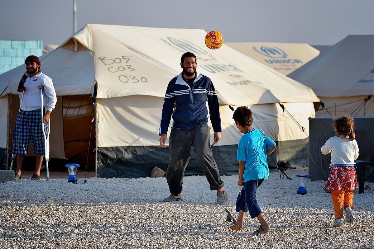 A man plays football with his children in the Zaatari Refugee Camp, Jordan, while another man, wounded in fighting in Syria, looks on. Photo: Paul Jeffrey/ACT